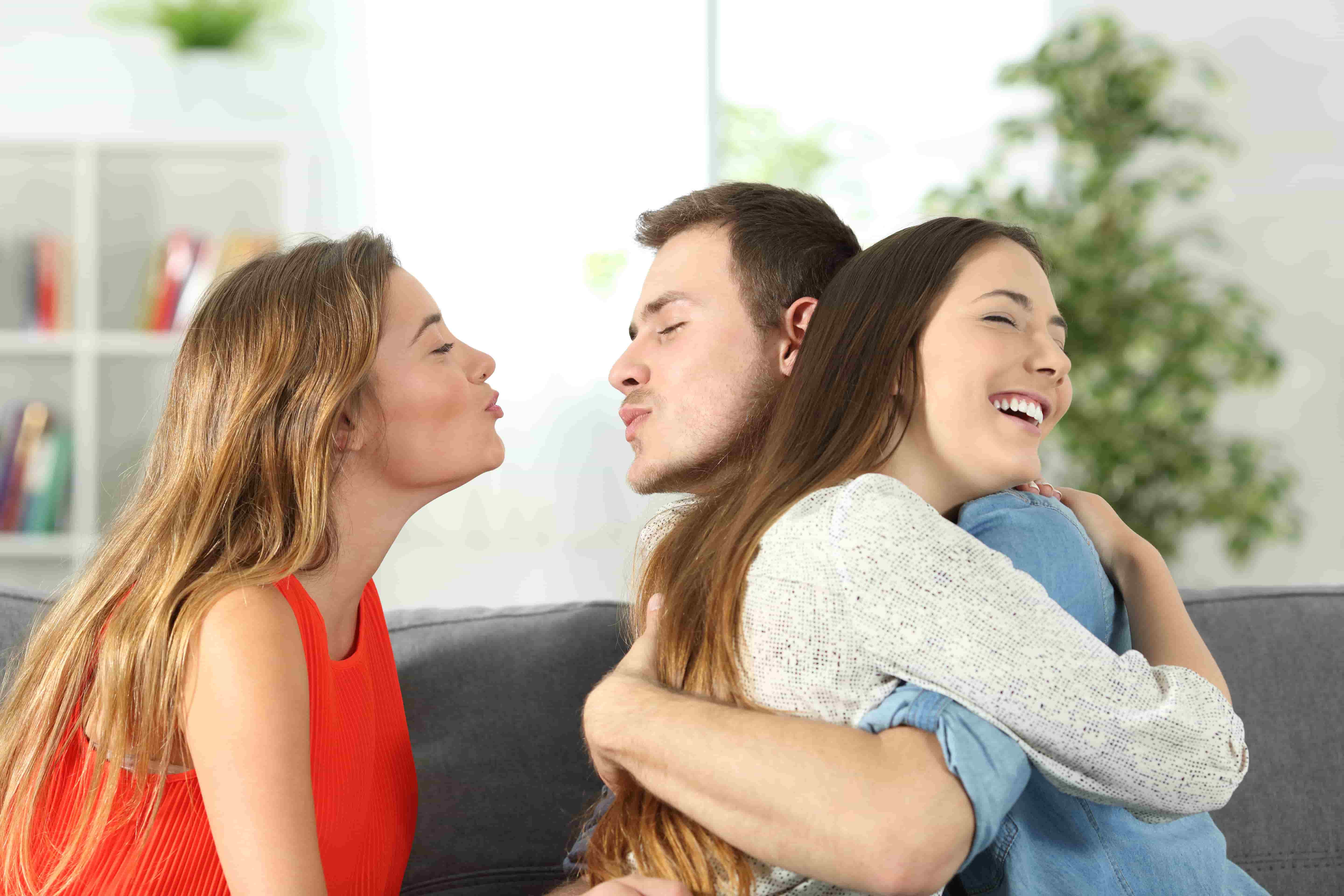 man hugging one woman while trying to kiss another